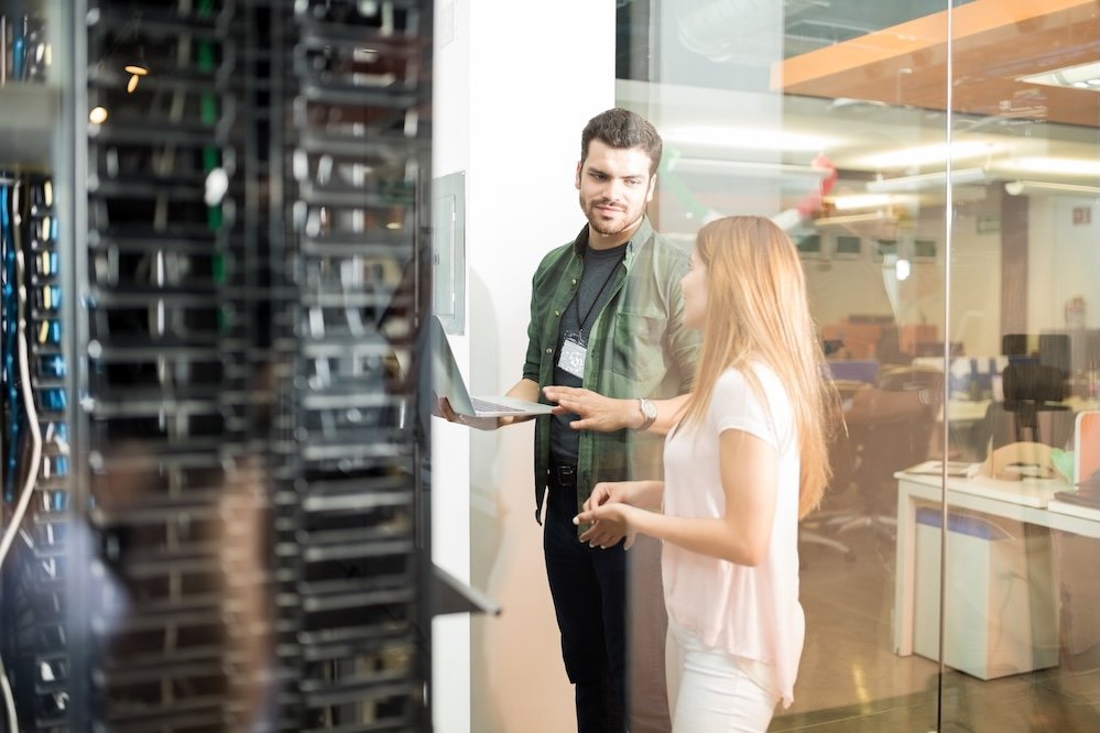 Two professionals collaborating with a laptop inside a server room